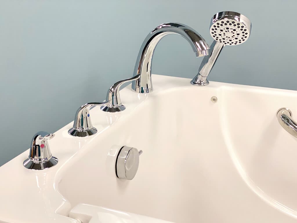 Chrome deck-mounted faucet and handheld showerhead on a white walk-in tub